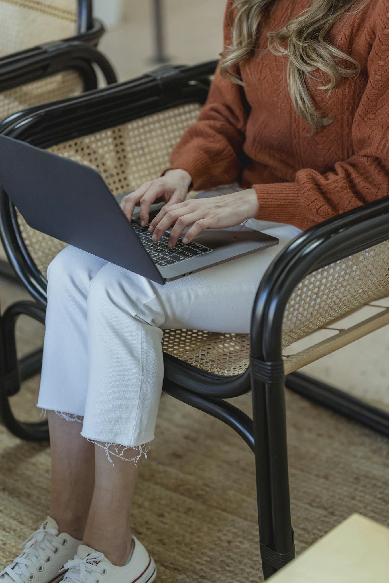 High angle of crop unrecognizable female remote employee sitting in armchair and typing on netbook while working online on startup